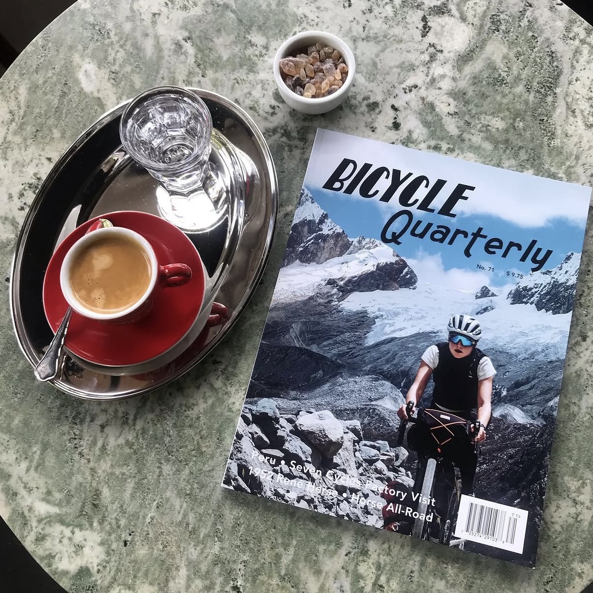 En espresso på silverbricka bredvid tidskriften Bicycle Quarterly på ett marmorbord